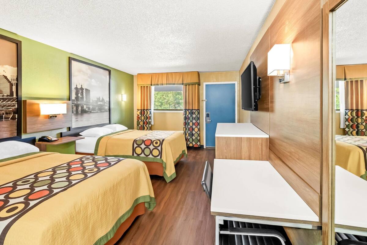 A hotel room with two beds, a TV, a desk, and a window with curtains.
