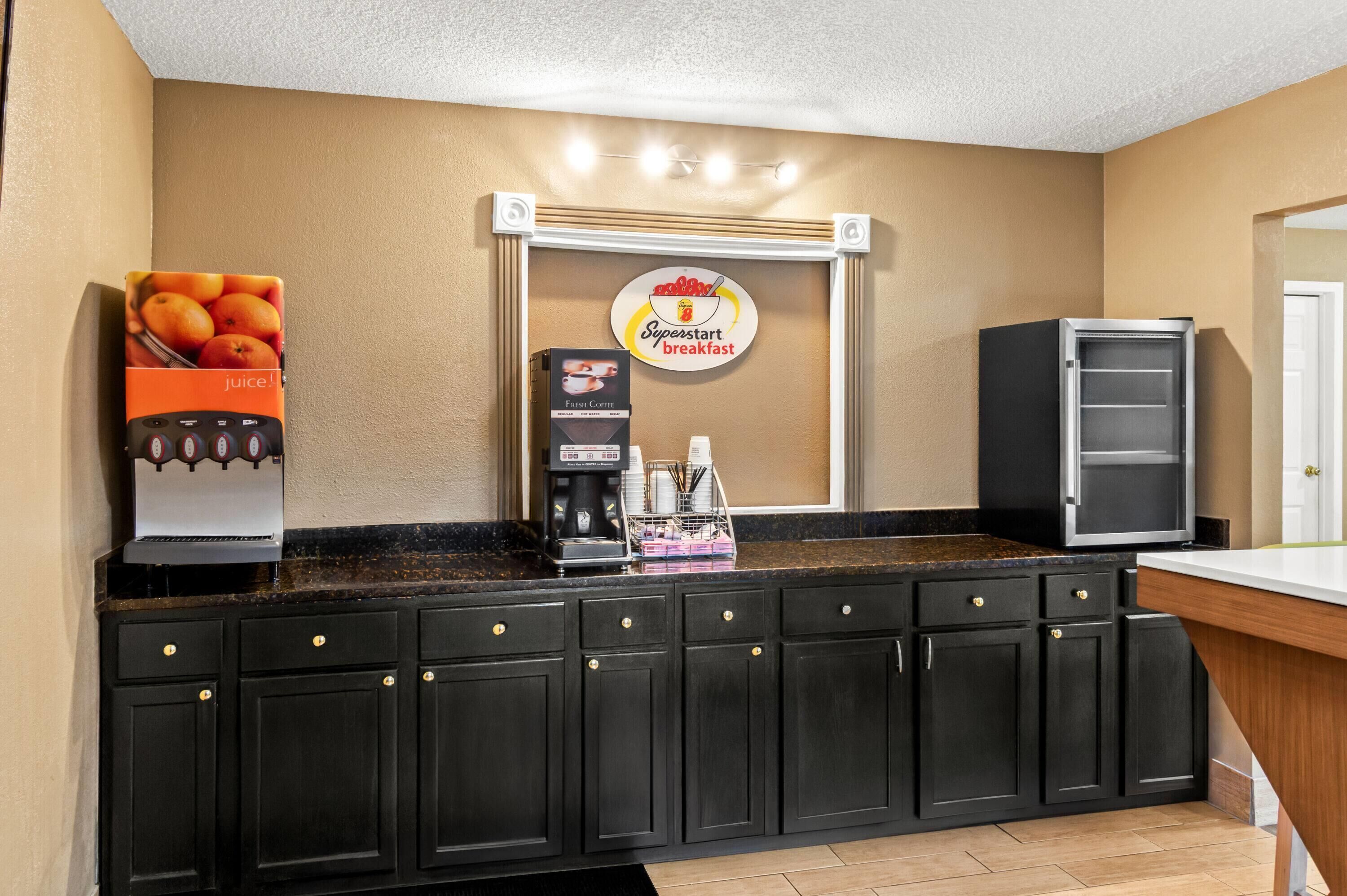 A kitchenette with a coffee machine, a juice dispenser, and a refrigerator.