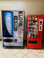 Two vending machines, one with a blue and black design and the other red, both stocked with snacks and drinks.