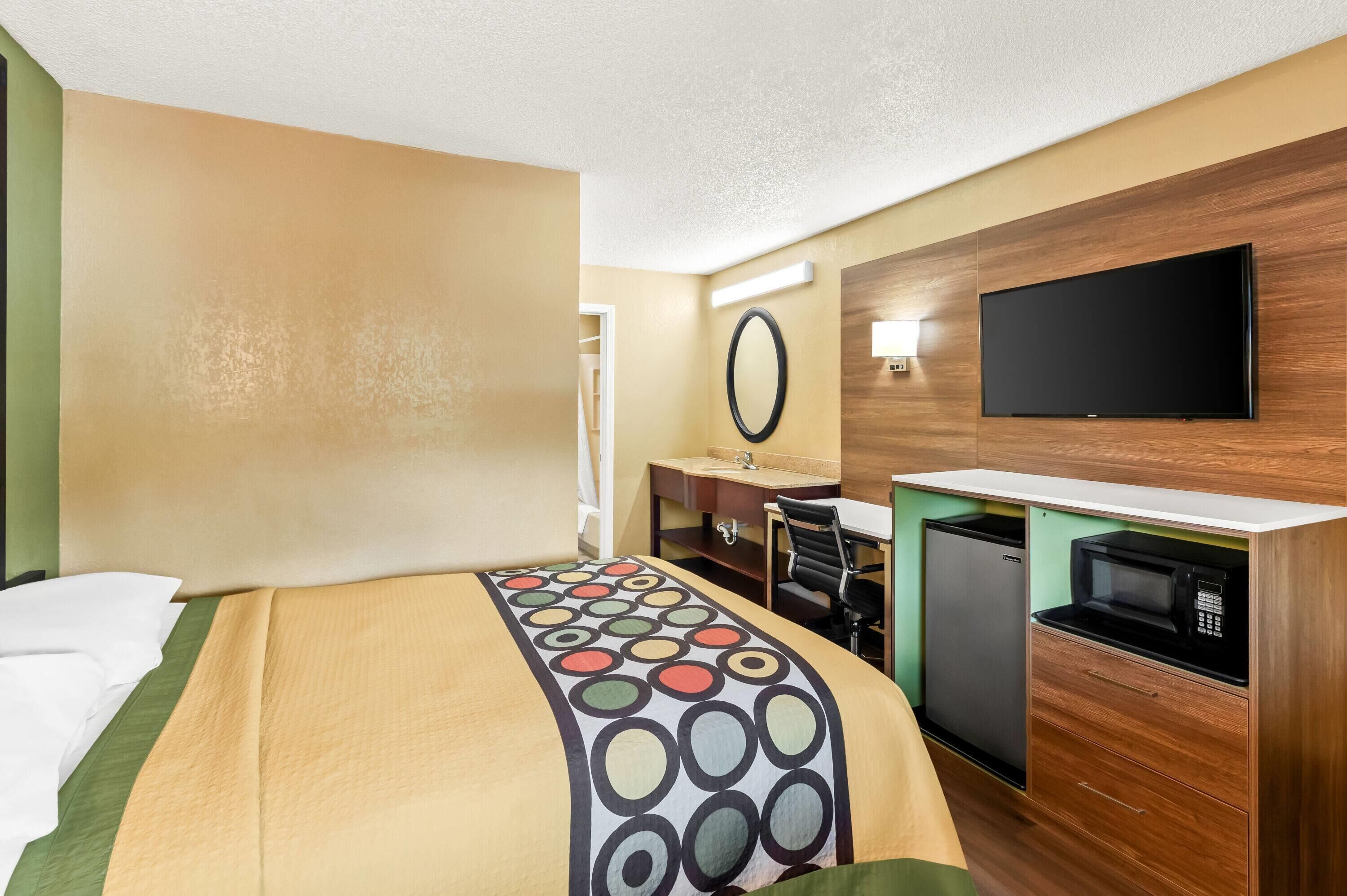 A hotel room with a bed, a desk, a microwave, and a television.
