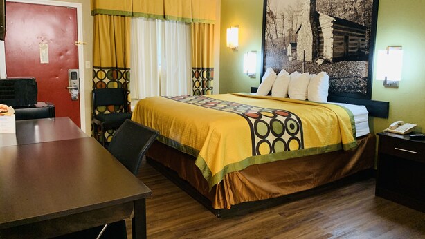 A hotel room with a bed, a desk, a chair, a red door, and a wall with a picture. - Super 8 by Wyndham Cincinnati/Springdale OH (Cincinnati)