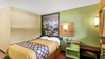 A hotel room with a bed, a wall-mounted lamp, a small wooden table, and a green shelf.