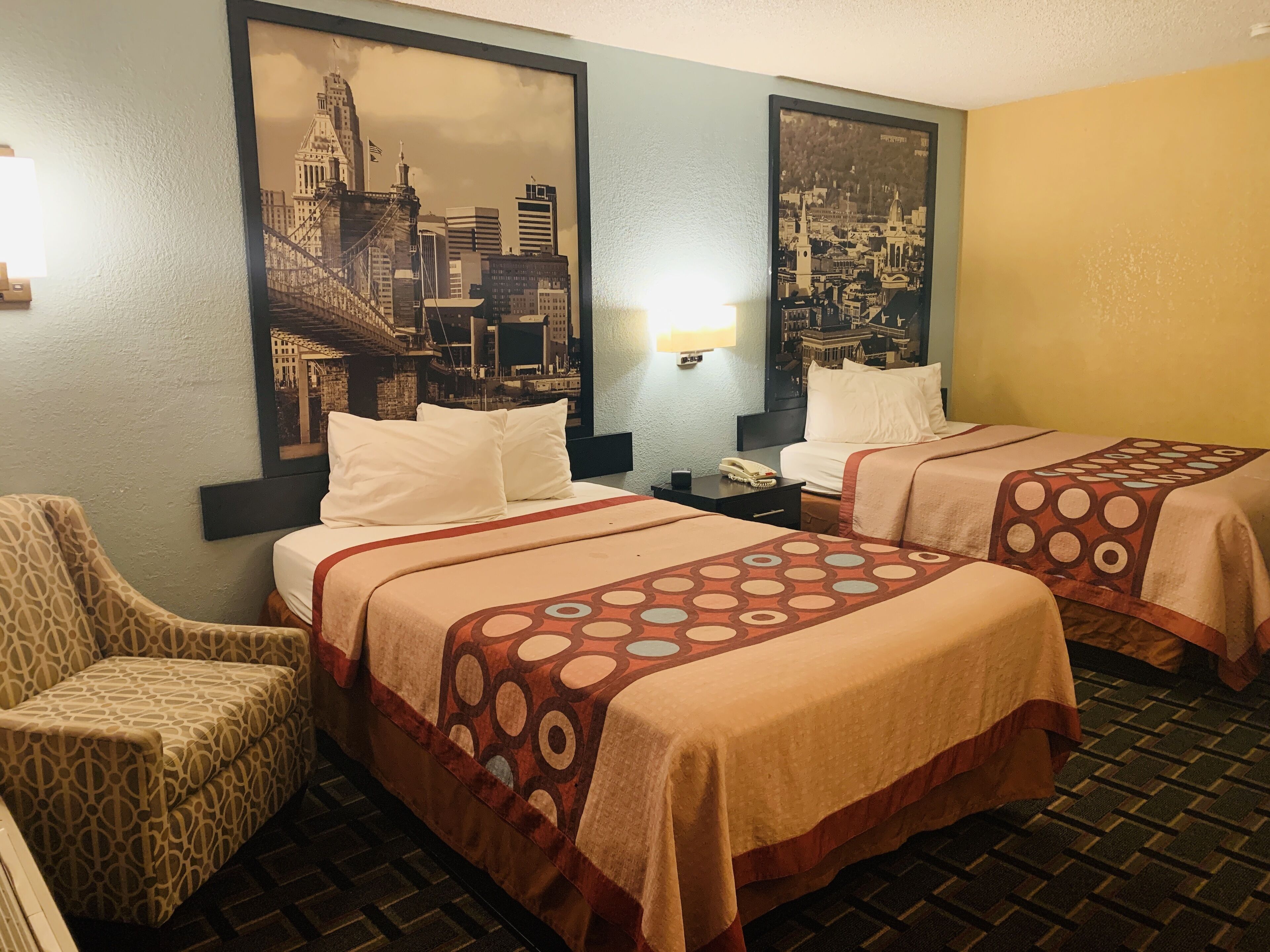 Une chambre d’hôtel avec deux lits, une chaise et deux grandes photos encadrées représentant des vues de la ville, accrochées aux murs.