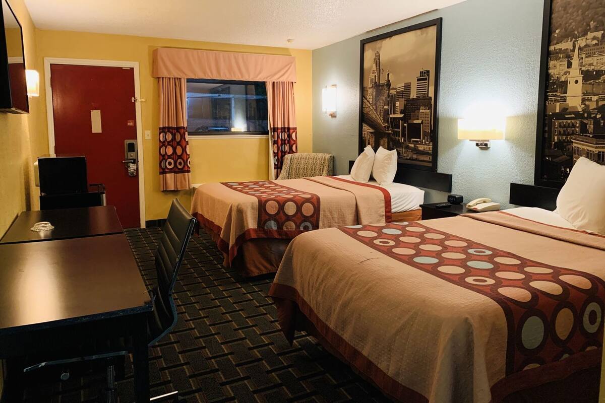 A hotel room with two beds, a desk, a chair, a door, and a window with curtains.