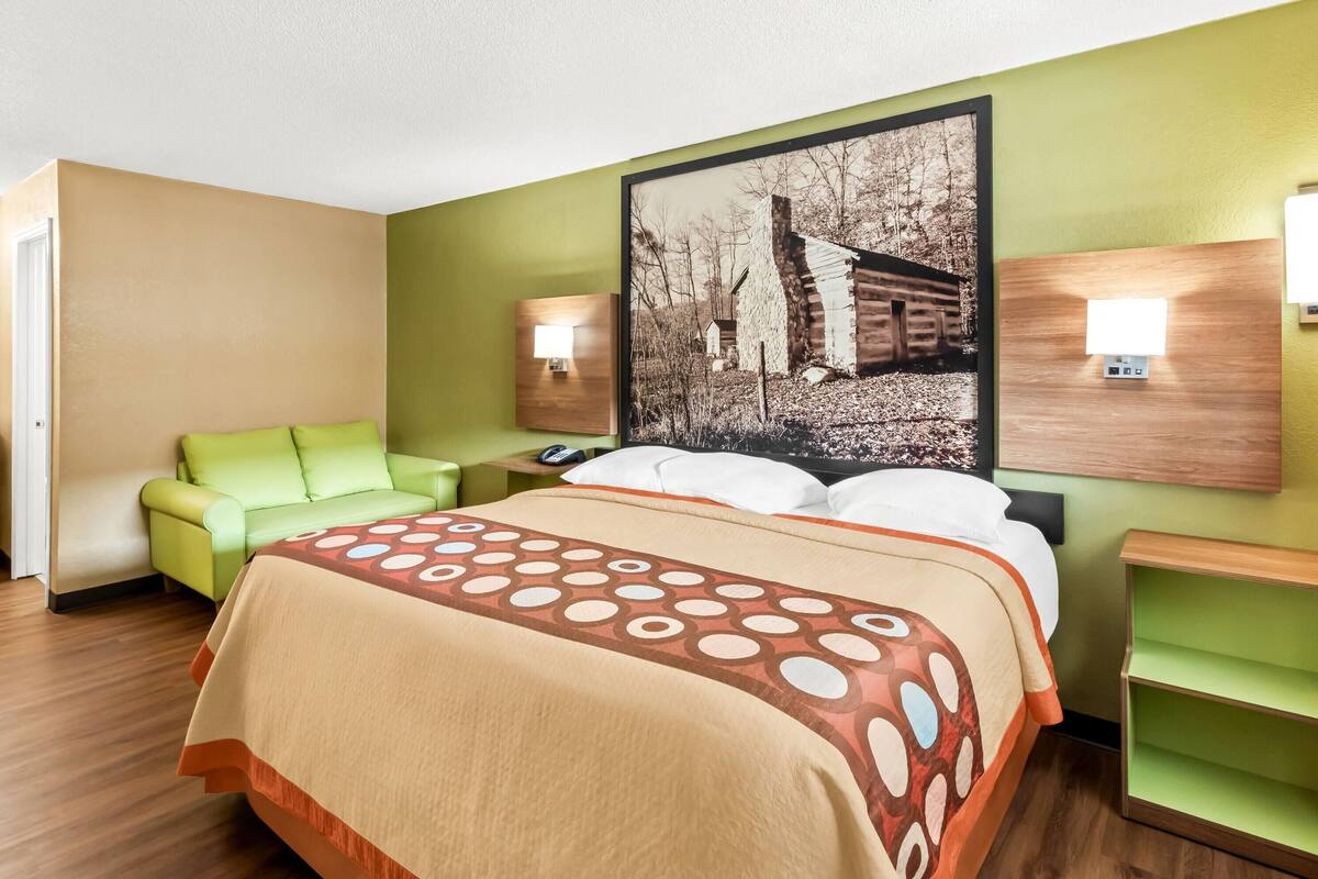 A hotel room with a bed, a green sofa, a nightstand, and a wall-mounted lamp.