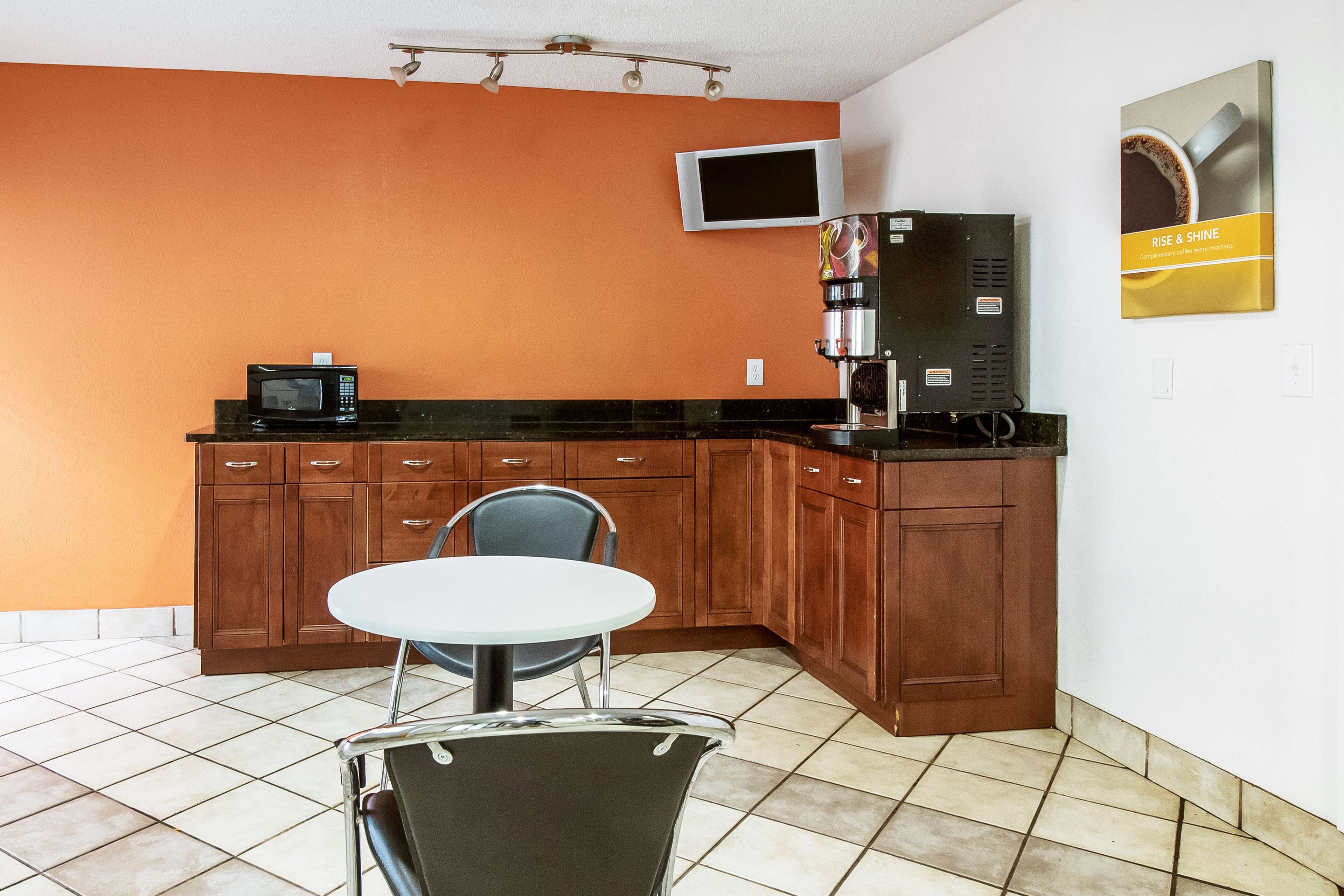 Una cocina compacta con microondas, cafetera y televisor montado en la pared.