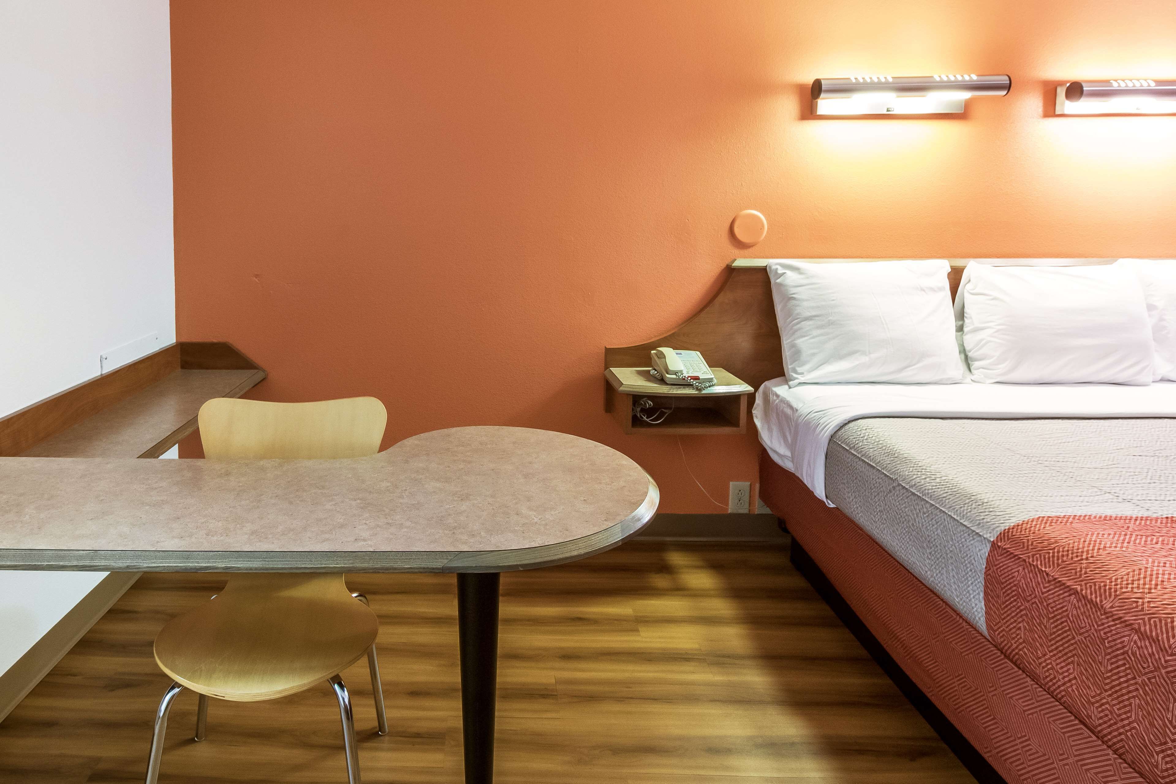 A hotel room with a bed, a bedside table with a lamp, a chair, and a small table.