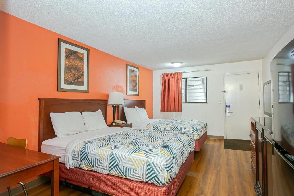 A hotel room with two beds, a desk, a television, and a door.