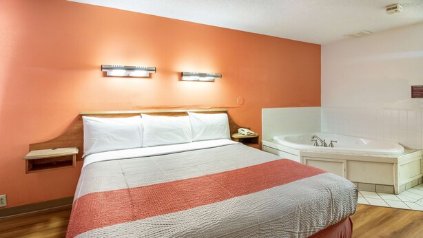 A hotel room with a bed, a nightstand, a telephone, and a bathroom with a bathtub. - Motel 6 Dayton, OH - Englewood (Englewood)