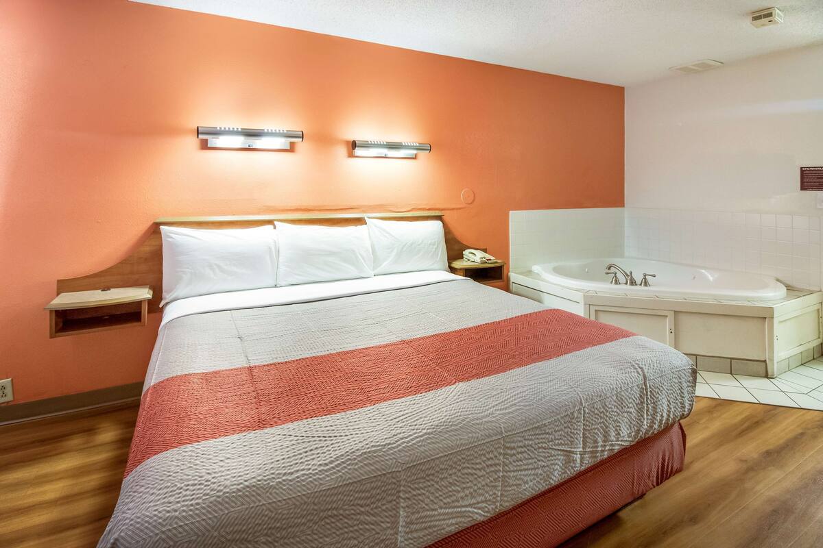 A hotel room with a bed, a nightstand, a telephone, and a bathroom with a bathtub.