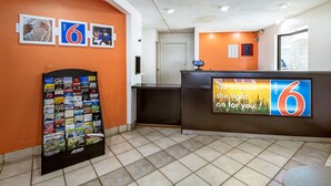 A motel lobby with orange walls, a reception desk, a vending machine, and a large sign with the number 6. - Motel 6 Dayton, OH - Englewood (Englewood)