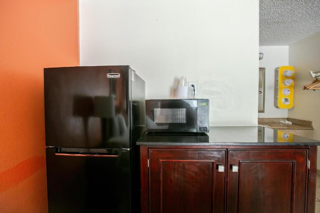 A kitchen with a black refrigerator, a microwave, and a wooden cabinet.
