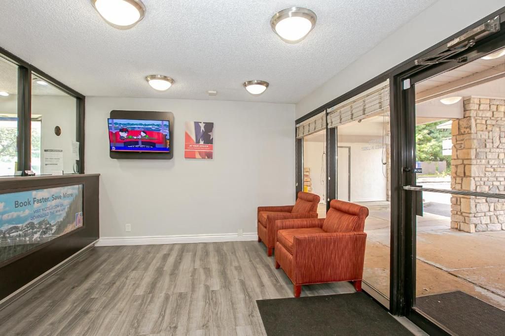 A reception area with a reception desk, two armchairs, a television mounted on the wall, and a stone wall outside.