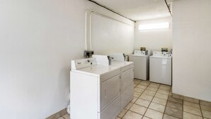 A laundry room with two washing machines and a dryer, white cabinets, and a tiled floor. - Motel 6 Dayton, OH - Englewood (Englewood)