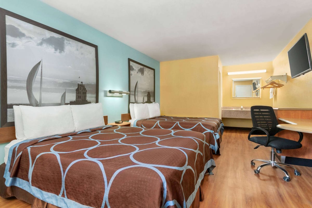 A hotel room with two beds, a desk, a chair, a TV, and artwork on the walls.