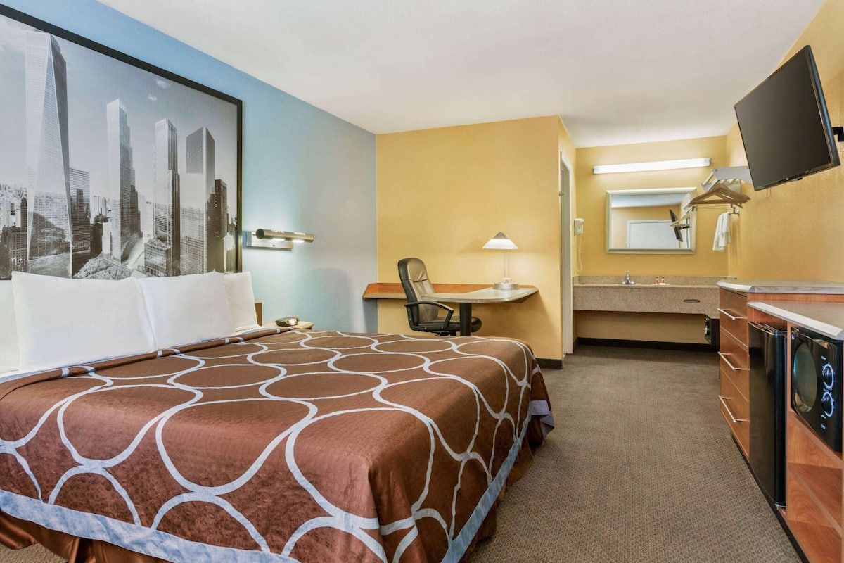 A hotel room with a bed, a desk with a chair, a bathroom with a mirror, and a television.
