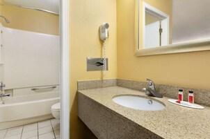 Baño con encimera de granito, lavabo, espejo, secador de pelo y ducha.