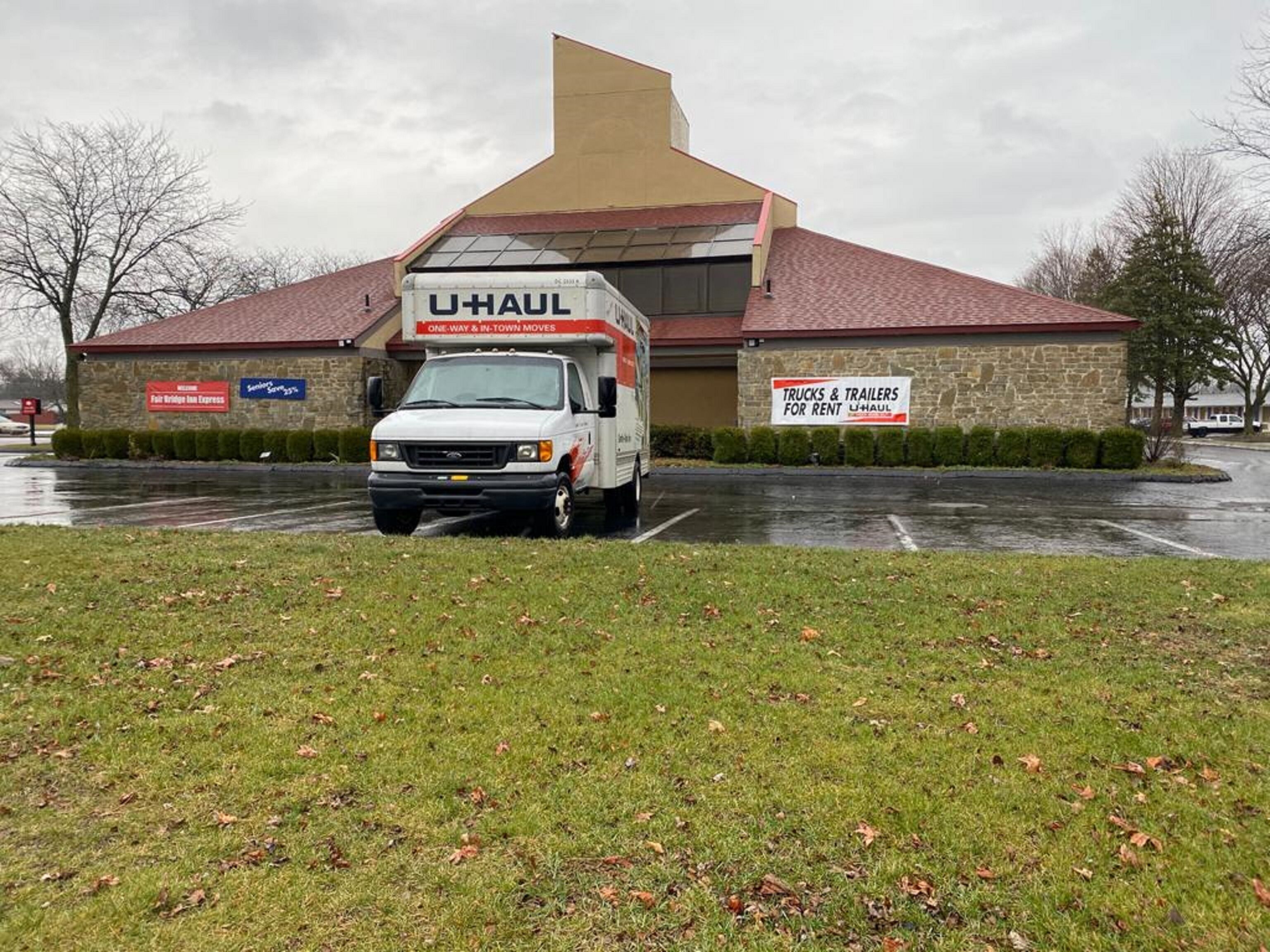 Un camión U-Haul estacionado en un estacionamiento, con un edificio al fondo.