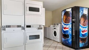 Ein Waschbereich mit gestapelten Waschmaschinen und Trocknern sowie einer Pepsi-Getränkeautomaten.