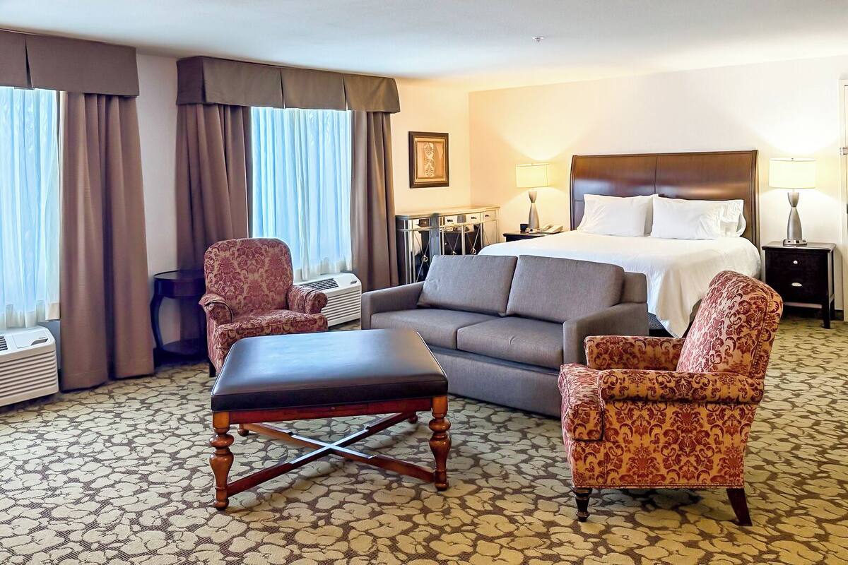 A hotel room with a bed, two armchairs, a sofa, a coffee table, and a desk with a lamp.