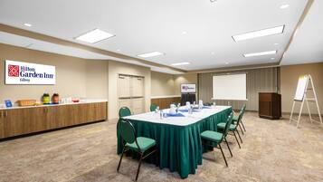 Uma sala de conferências com uma mesa comprida, cadeiras verdes, um quadro branco e um pódio.