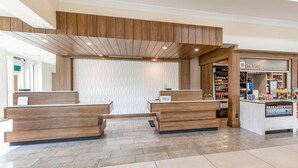 A hotel reception area with wooden reception desks, a patterned wall, and a shop named "The Shop" in the background.