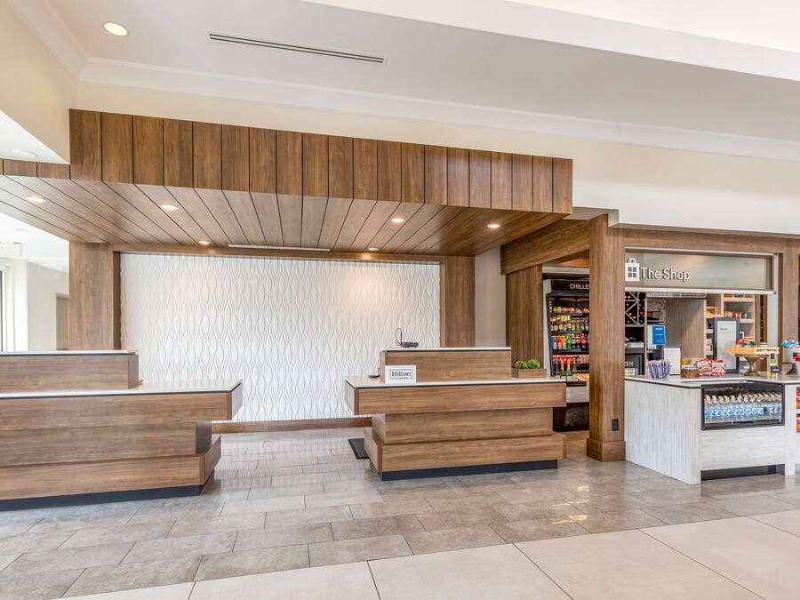 A hotel reception area with wooden reception desks, a patterned wall, and a shop named "The Shop" in the background.