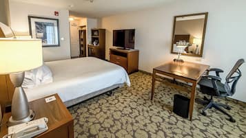 A hotel room with a bed, desk, chair, lamp, TV, and a patterned carpet.