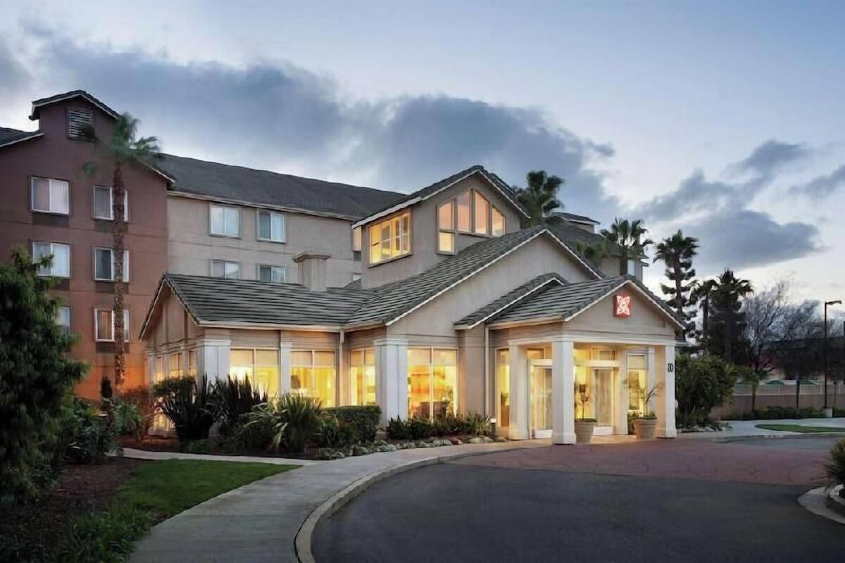 A multi-story hotel with a central entrance, large windows, and a landscaped driveway.