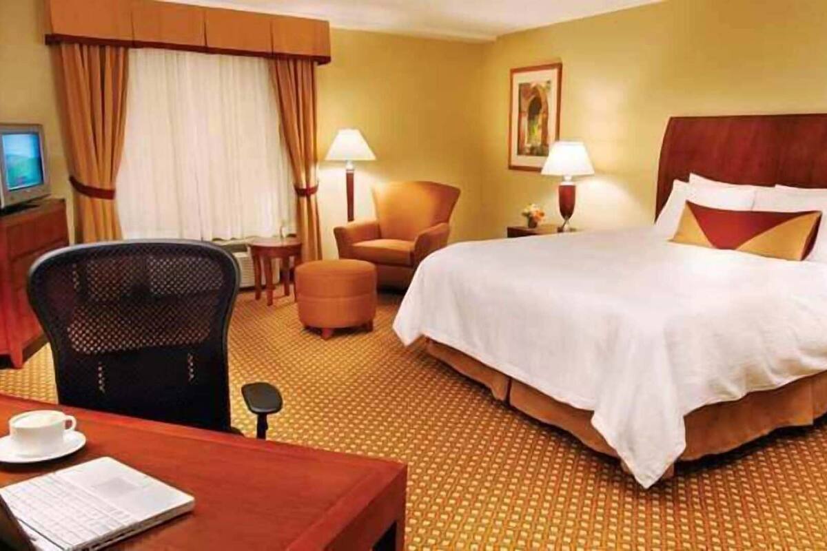 A hotel room with a bed, a desk with a chair, a small table, and a television.