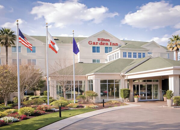 A Hilton Garden Inn with a modern design, featuring a large entrance with a covered walkway, multiple flags, and well-maintained landscaping.