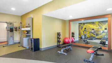 Un gimnasio con equipamiento de ejercicio, una banca y un espejo grande.