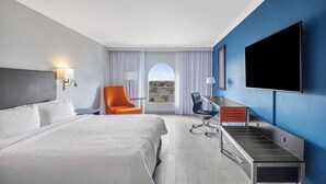 A hotel room with a bed, a desk, an orange chair, a TV, and a view of the outdoors. - Fiesta Inn Express Nuevo Laredo (Nuevo Laredo)