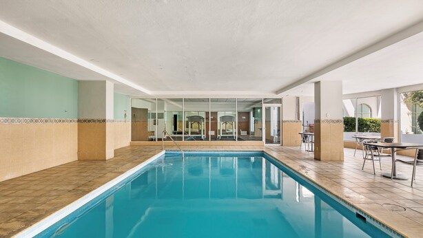 An indoor swimming pool with clear glass walls, a tiled floor, and a view of the outside. - Fiesta Inn Express Nuevo Laredo (Nuevo Laredo)