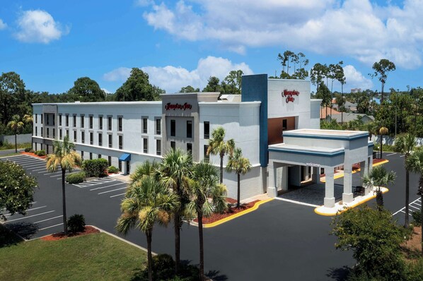 A hotel with a modern design, featuring a central entrance, a parking lot, and surrounding greenery. - Hampton Inn Panama City Beach (Panama City Beach)