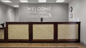 A reception desk with a "Welcome to the Sun Shine State" sign, a clock, and a "Hilton Honors" plaque. - Hampton Inn Panama City Beach (Panama City Beach)