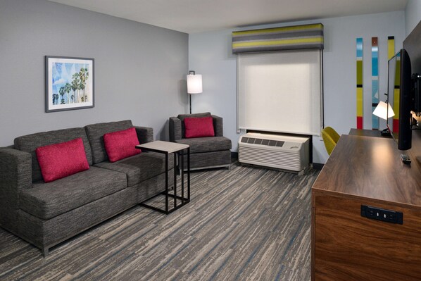 Una habitación de hotel moderna con un sofá gris, una mesita pequeña, un calentador portátil y un escritorio de madera.