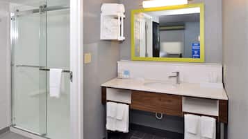 A modern bathroom with a glass shower enclosure, a sink with a wooden vanity, and a mirror with a yellow frame.