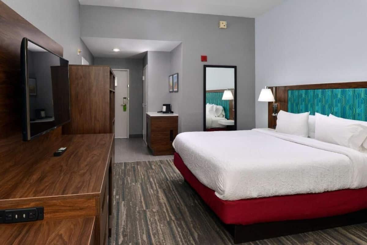 A hotel room with a bed, a TV, a desk, and a mirror.
