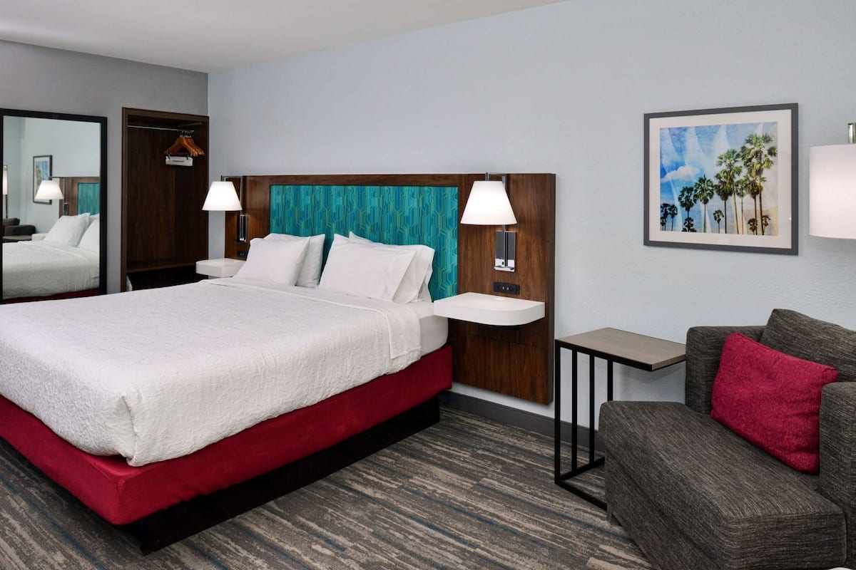 A hotel room with a bed, bedside tables, a nightstand, a sofa, and a painting on the wall.