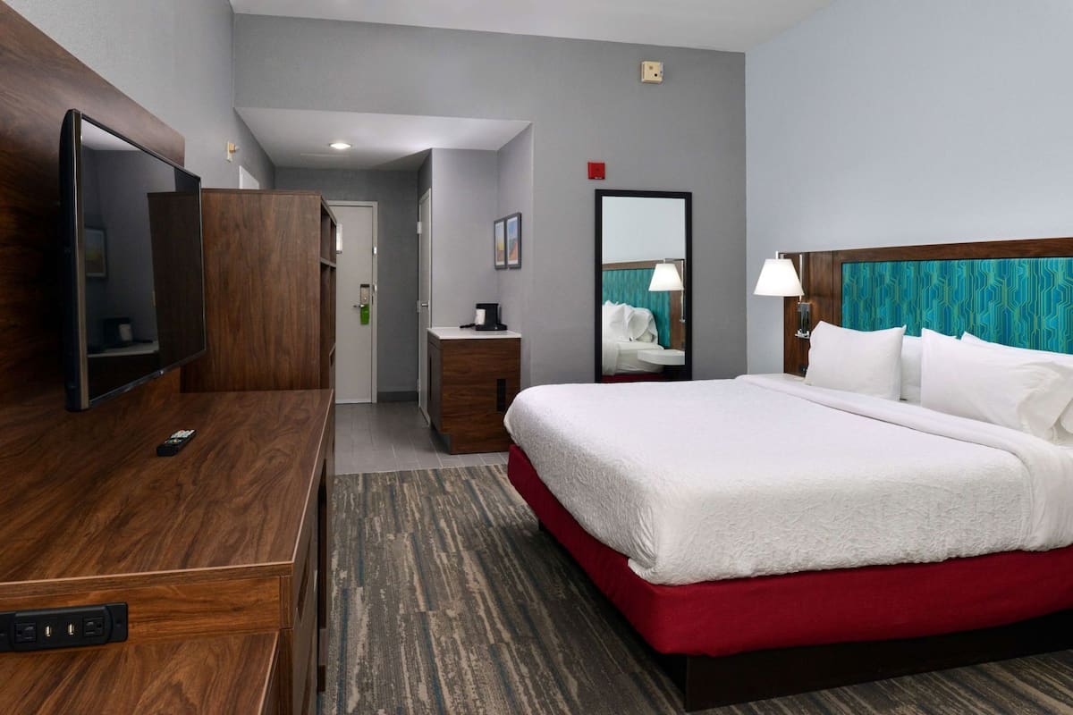 A hotel room with a bed, a desk, a TV, a mirror, and a bathroom door.