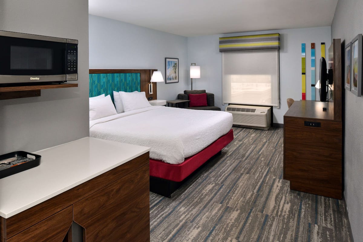 A hotel room with a bed, a desk, a microwave, a TV, and a window with curtains.
