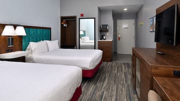 A hotel room with two beds, a desk, a TV, a mirror, and a small kitchenette.