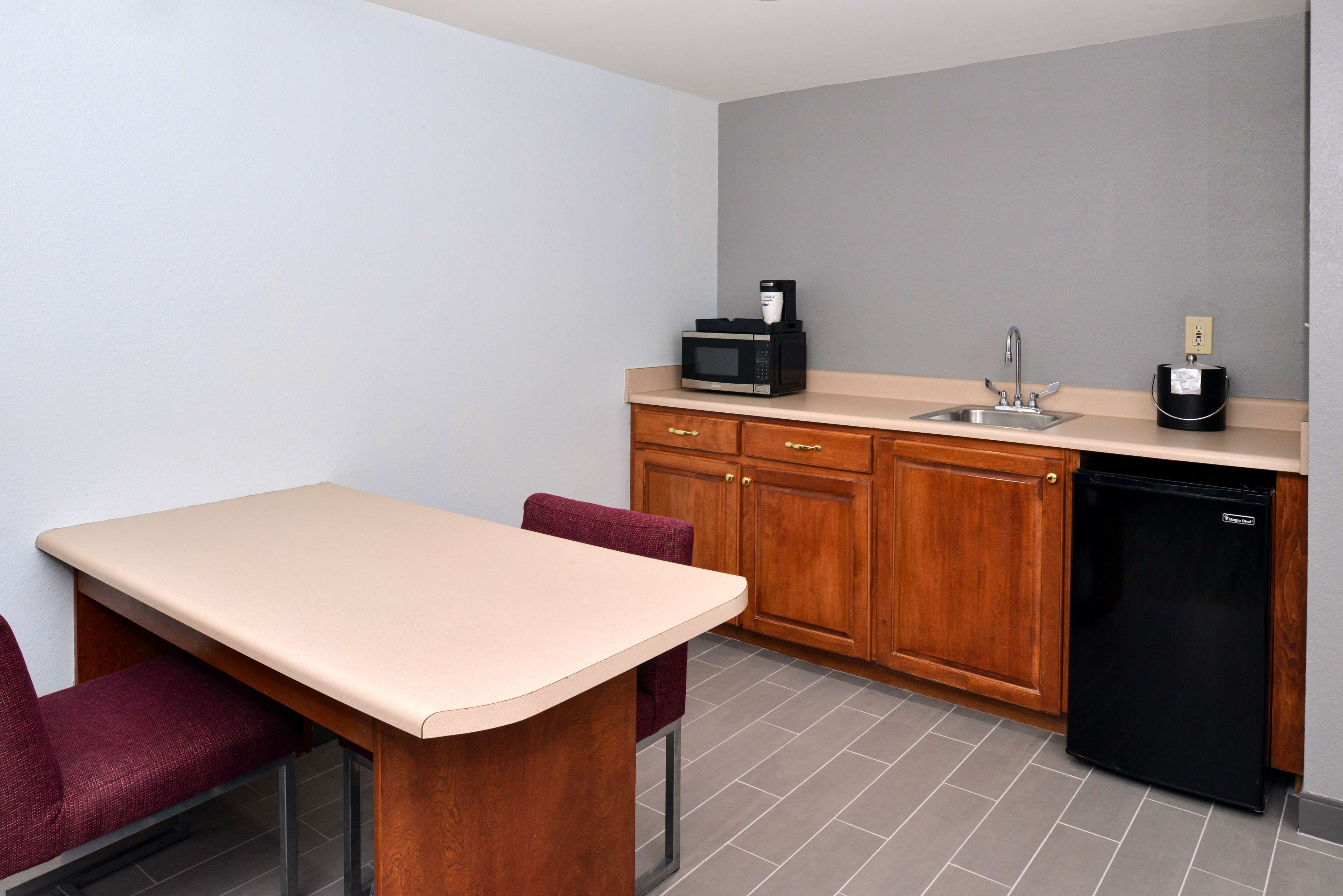 A compact kitchen with a wooden cabinet, a black refrigerator, a microwave, and a sink.
