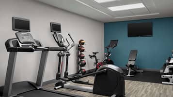 Un gimnasio con equipo cardiovascular, máquinas de pesas y una pantalla de televisión.