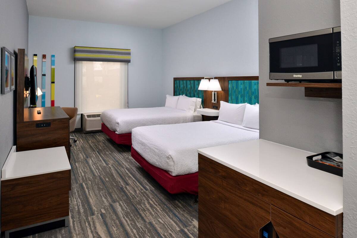 A hotel room with two beds, a desk, a microwave, and a TV.