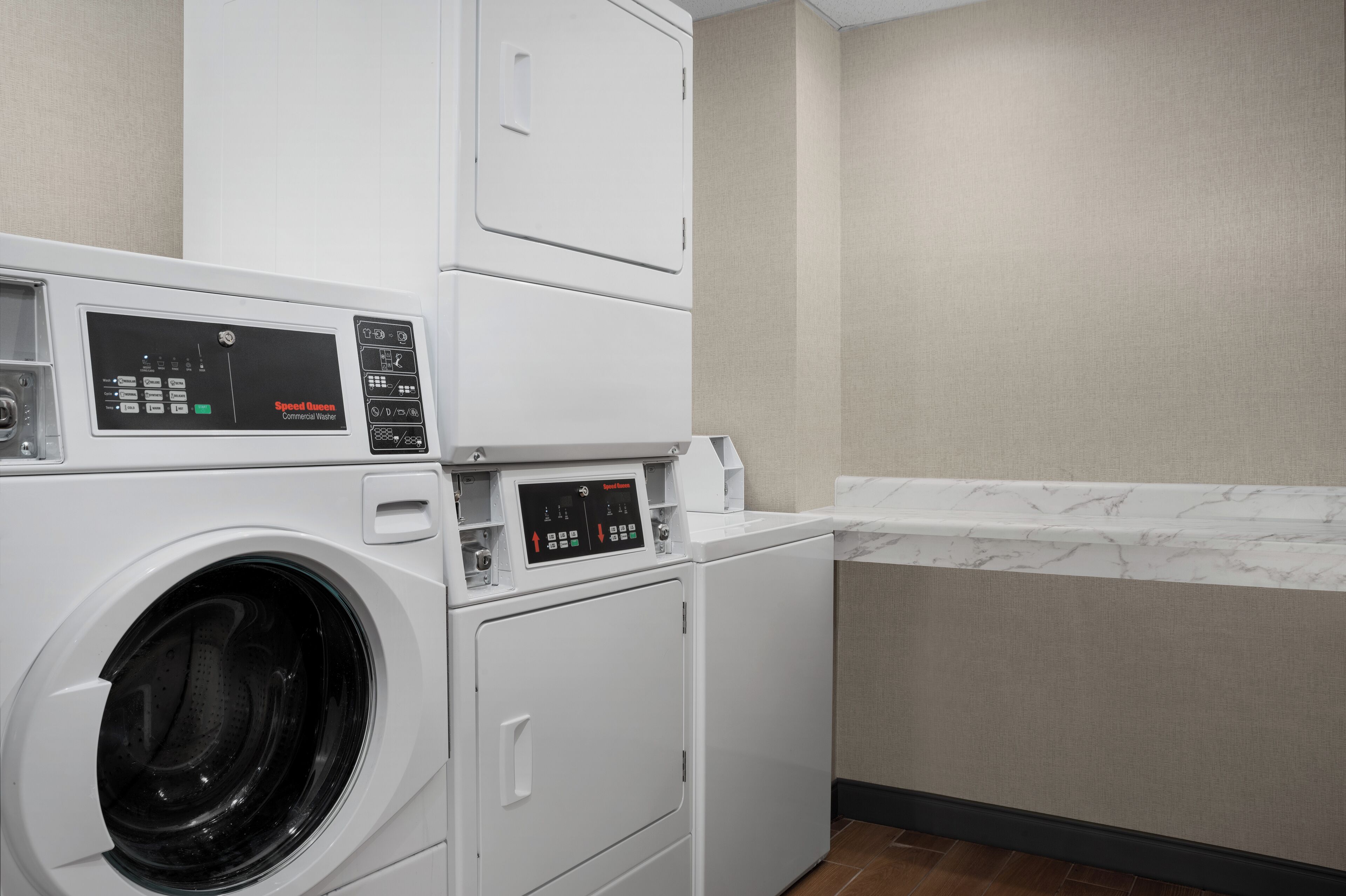 A laundry area with a front-loading washer and dryer, a control panel, and a marble countertop.
