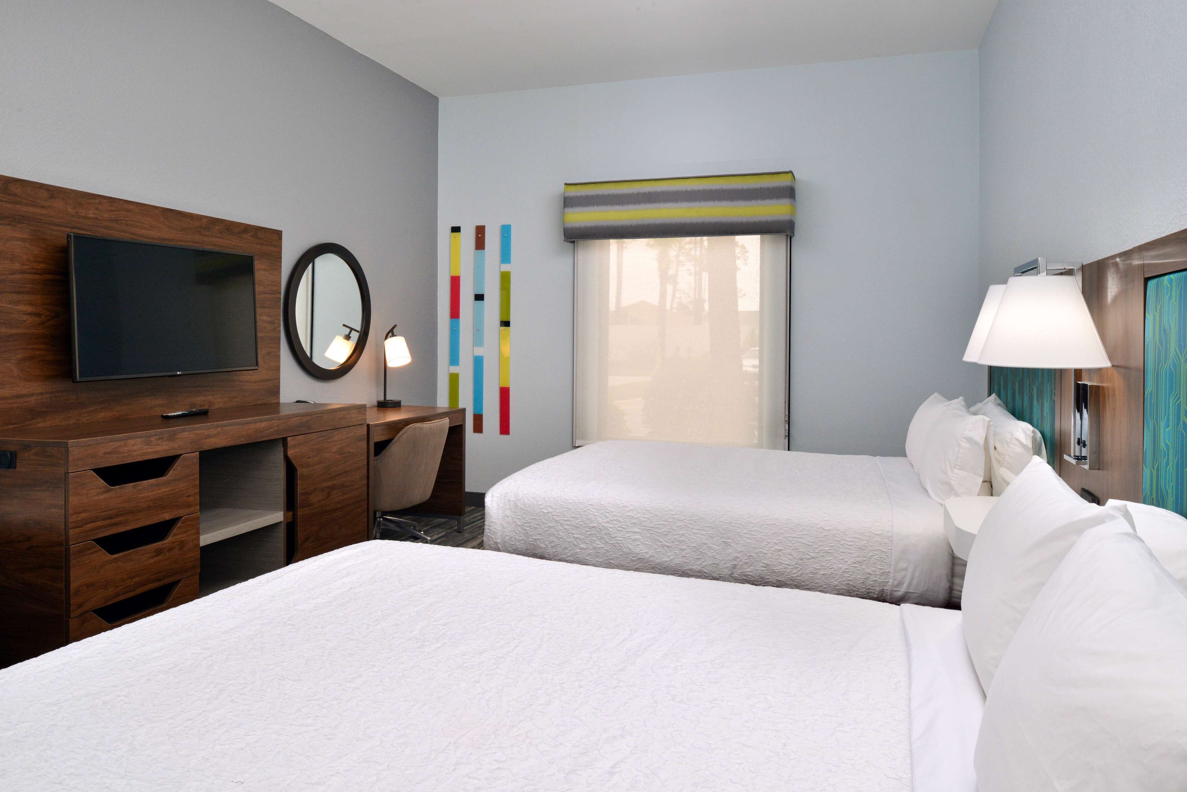 A hotel room with two beds, a desk, a TV, a lamp, and a window with a view.