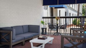 A balcony with a white brick wall, a gray sofa, a chessboard, and outdoor furniture. - Hampton Inn Panama City Beach (Panama City Beach)