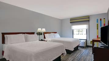 A hotel room with two beds, a TV, a desk, and a window with a view.